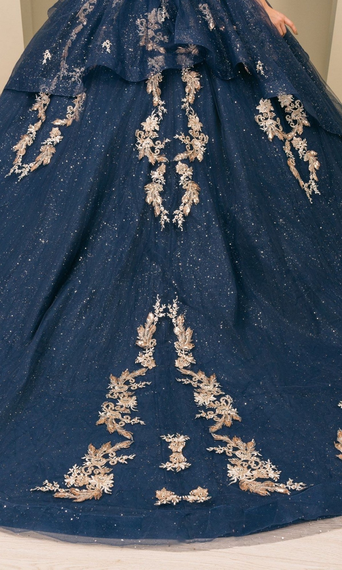 A stunning navy blue quinceanera ball gown, Quinceanera Dress 8390JQ by Cinderella Couture, features gold floral embroidery cascading down the skirt and sparkly details, shown from the waist down.
